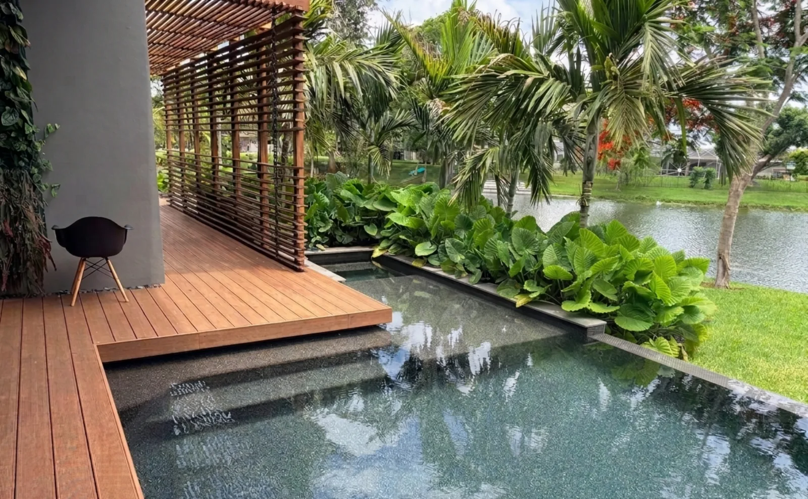 Pool with slatted wood pergola and tropical plants next to the lake | FDS Pools